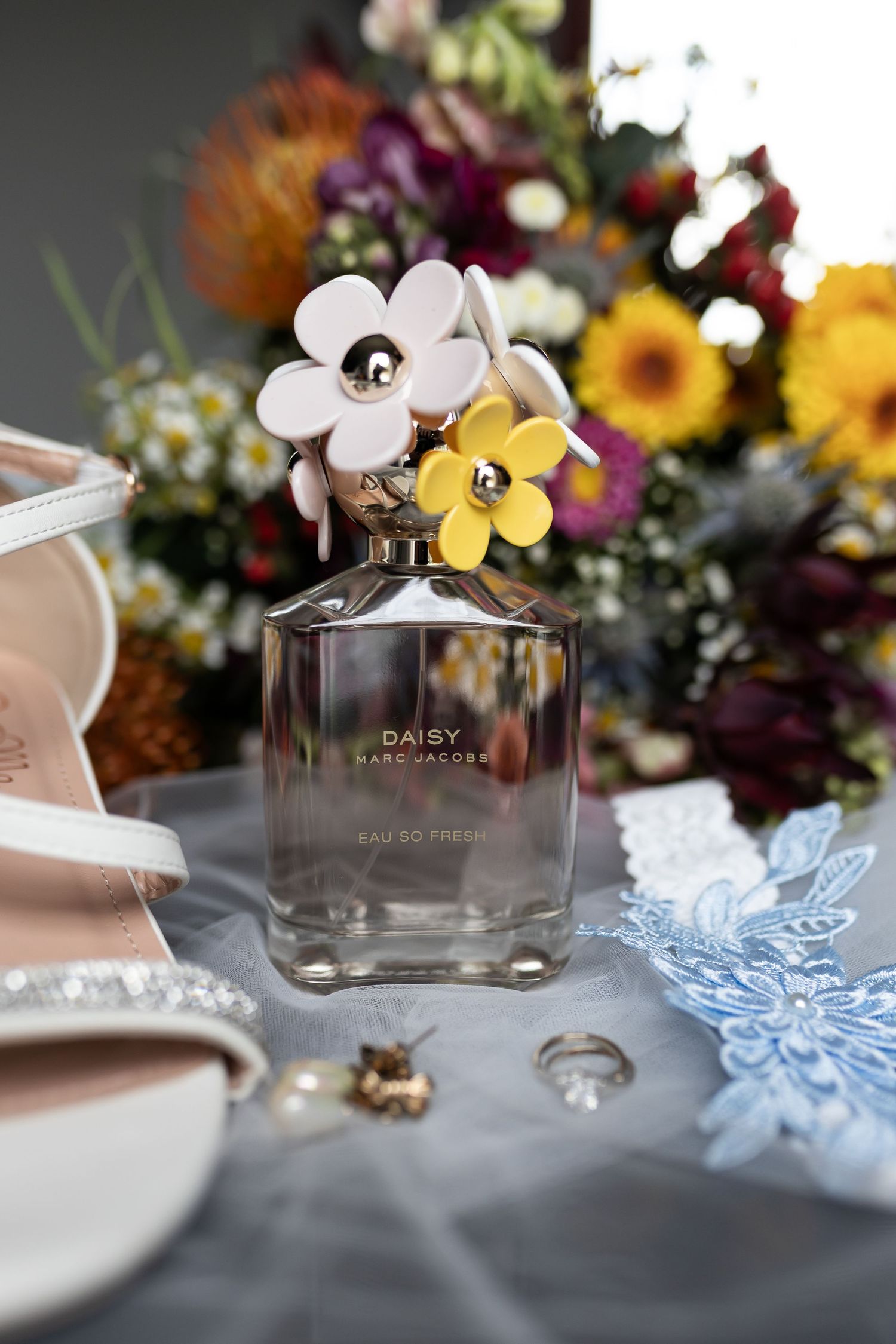Marc Jacobs Daisy perfume bottle with floral decorations displayed among colorful flowers.