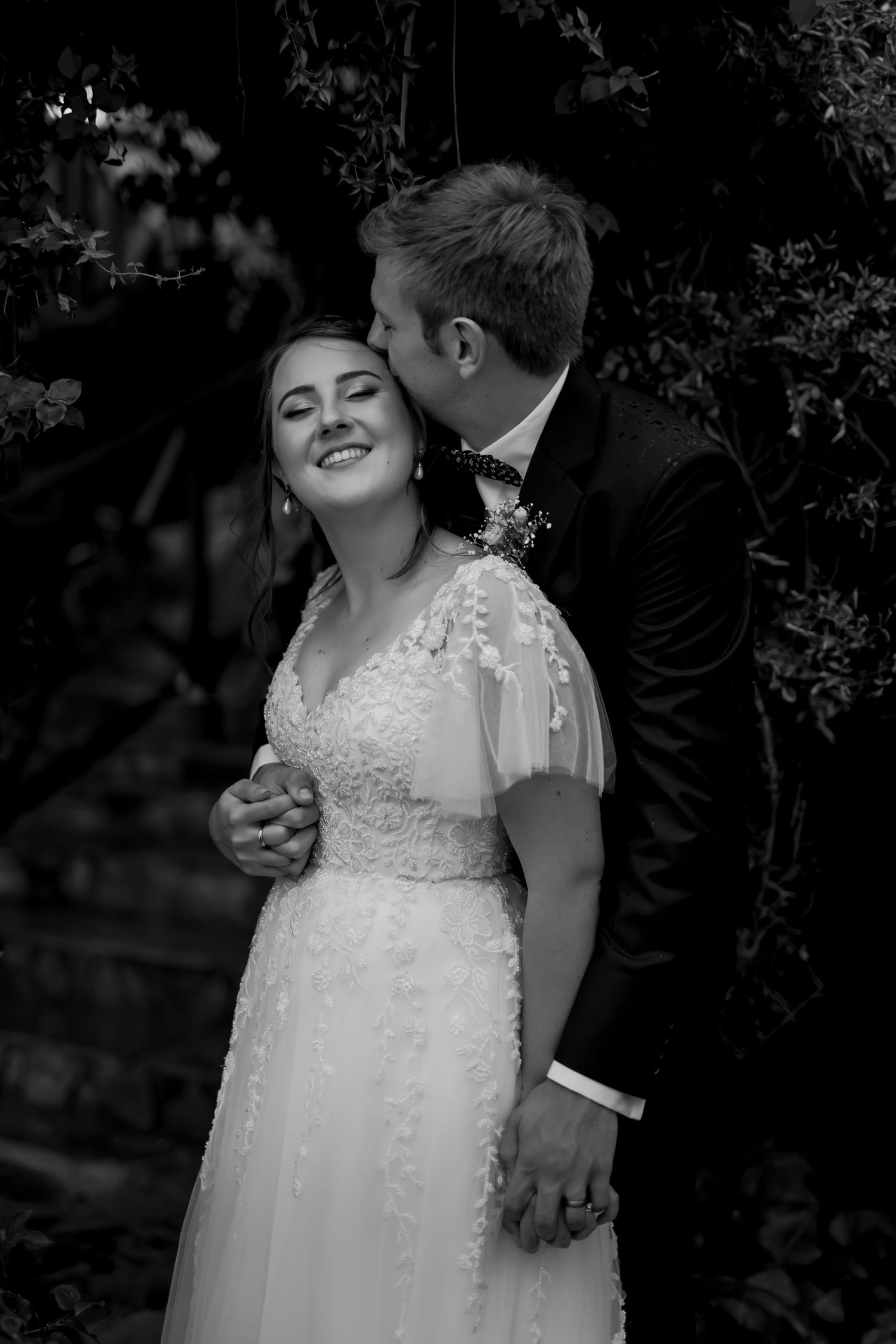 Black and white wedding portrait showing tender moment in garden setting.