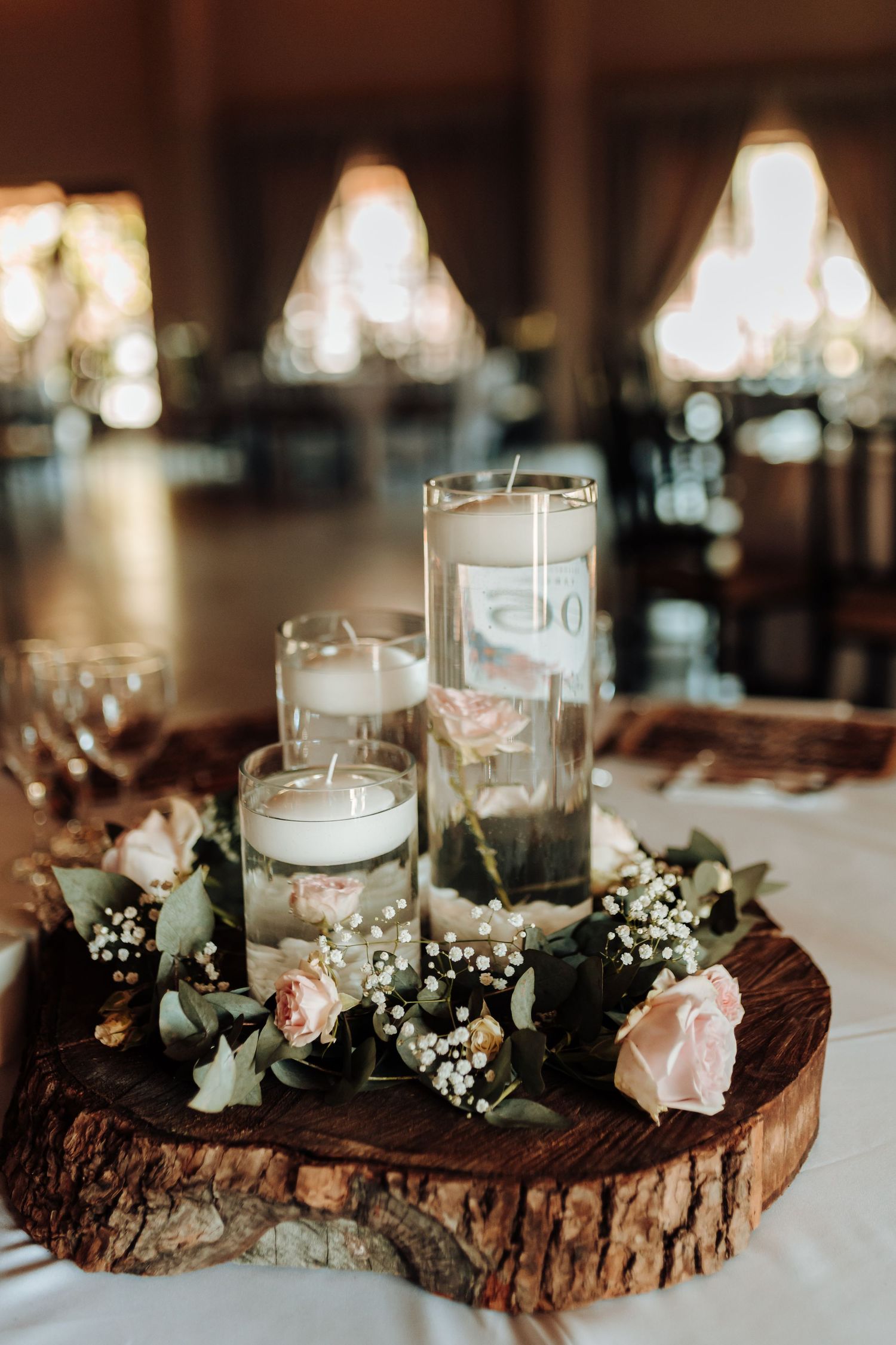 Rustic wedding centerpiece with floating candles and roses on wood slice base.