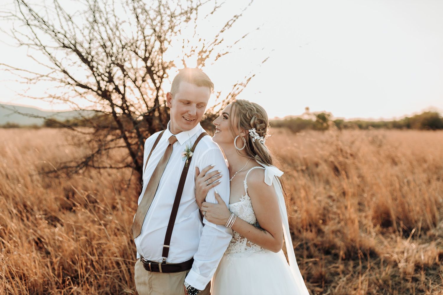 Intimate wedding portrait captured in warm sunset light among dried grass field.