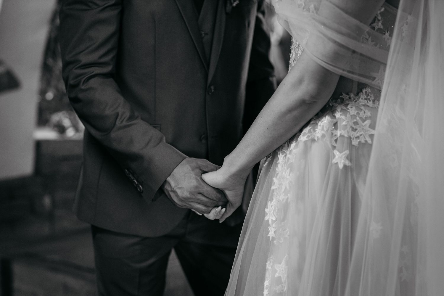 Close-up of bride and groom holding hands during wedding ceremony in black and white.