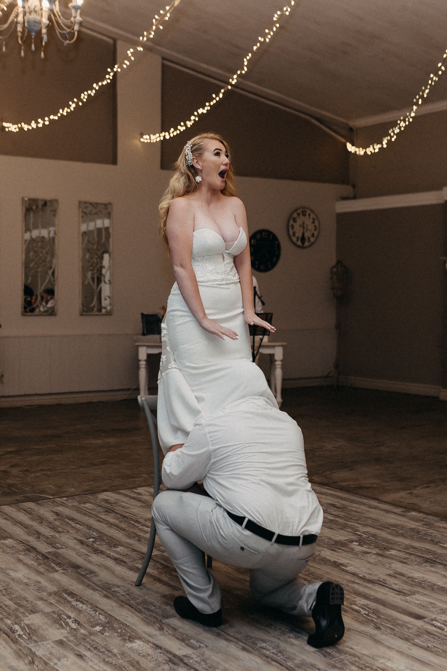 A playful moment during a wedding reception with string lights decorating the ceiling.