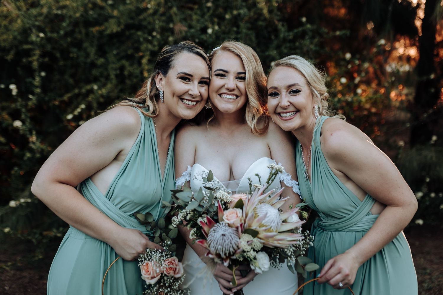 Three women in mint green and white dresses holding bouquets and smiling together.