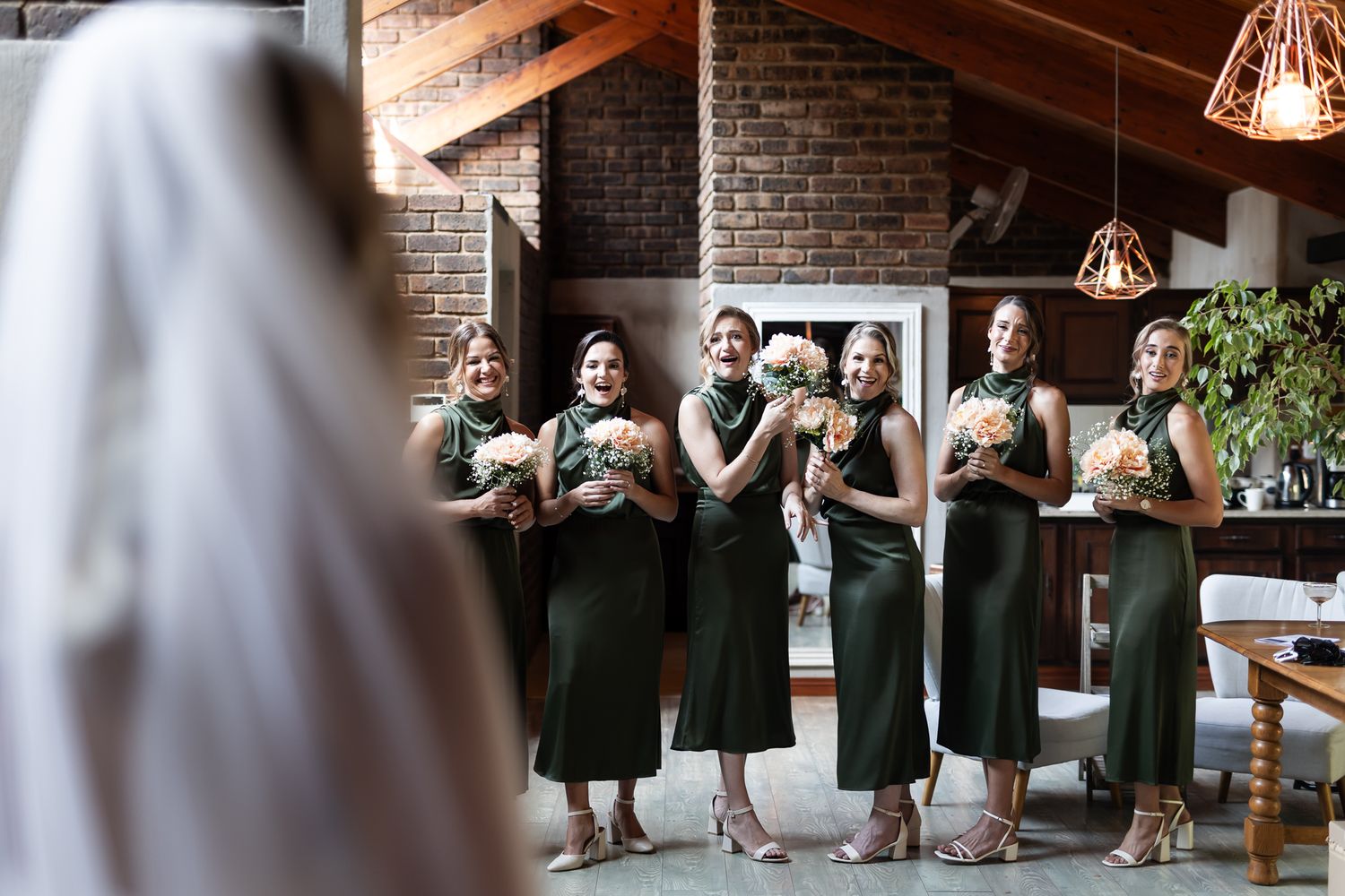 Bridesmaids in matching green dresses react emotionally to bride's first look reveal.