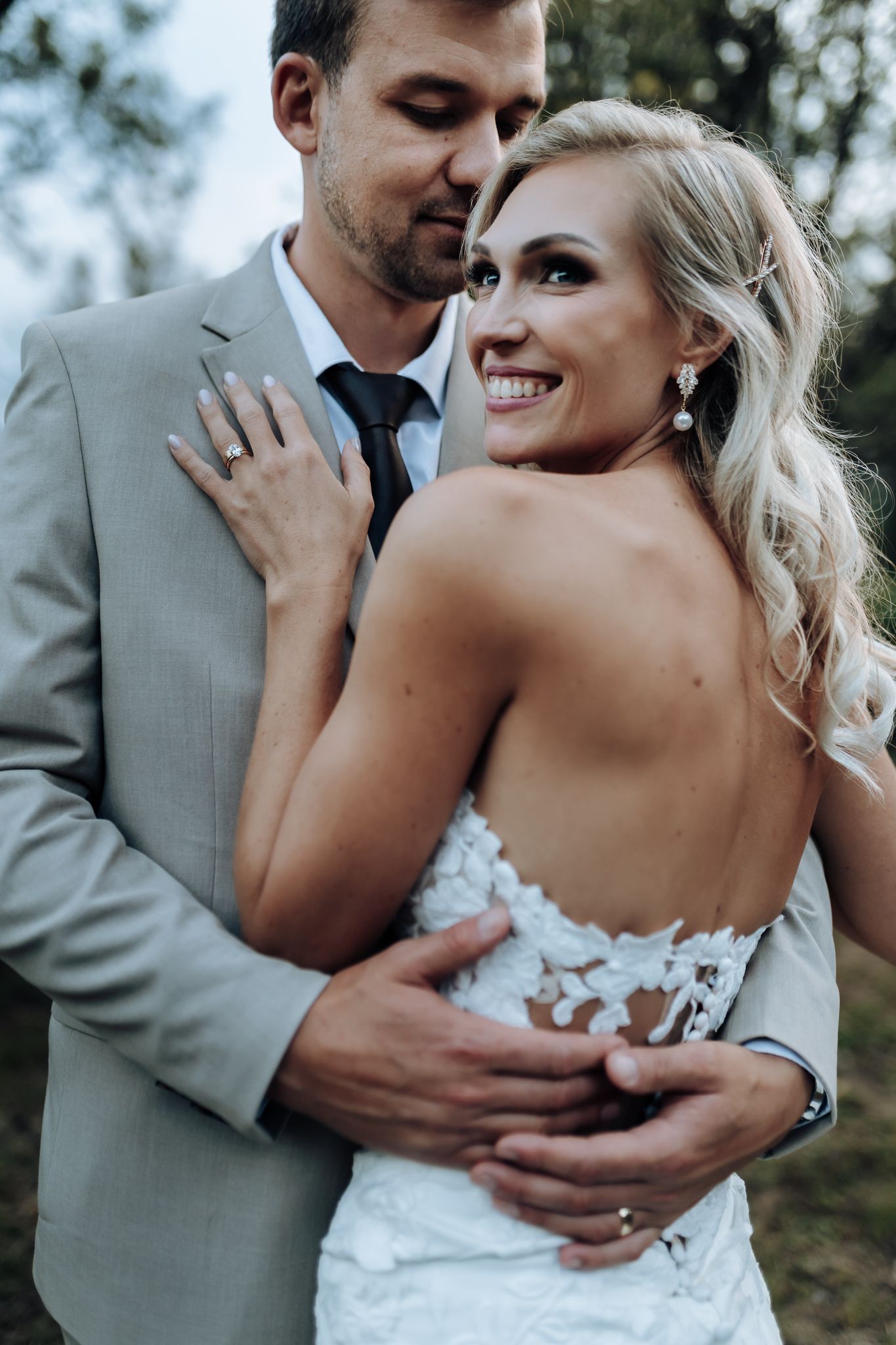 Intimate wedding portrait in elegant attire against natural outdoor setting.