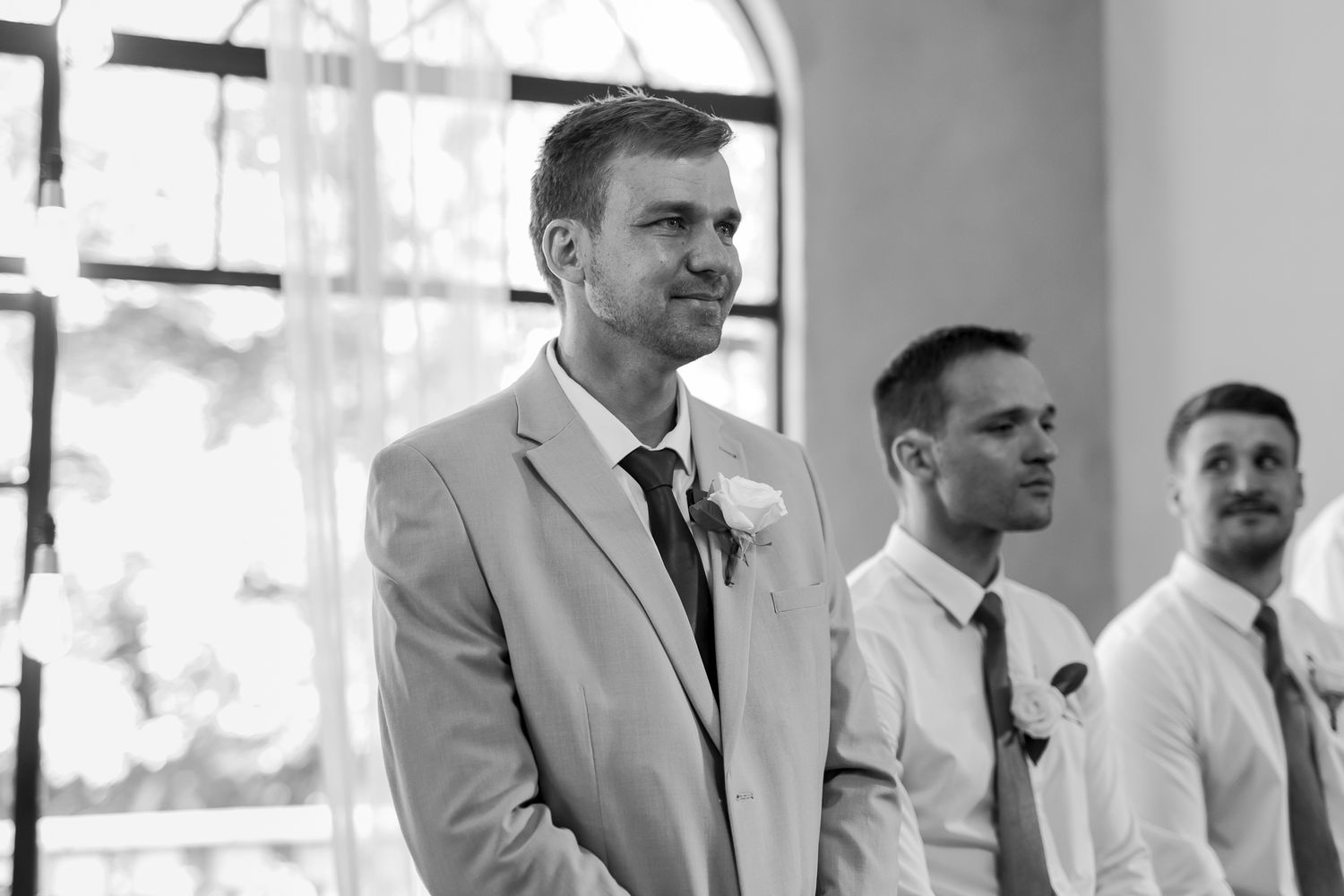 Black and white photo of groomsmen standing at altar during indoor ceremony.