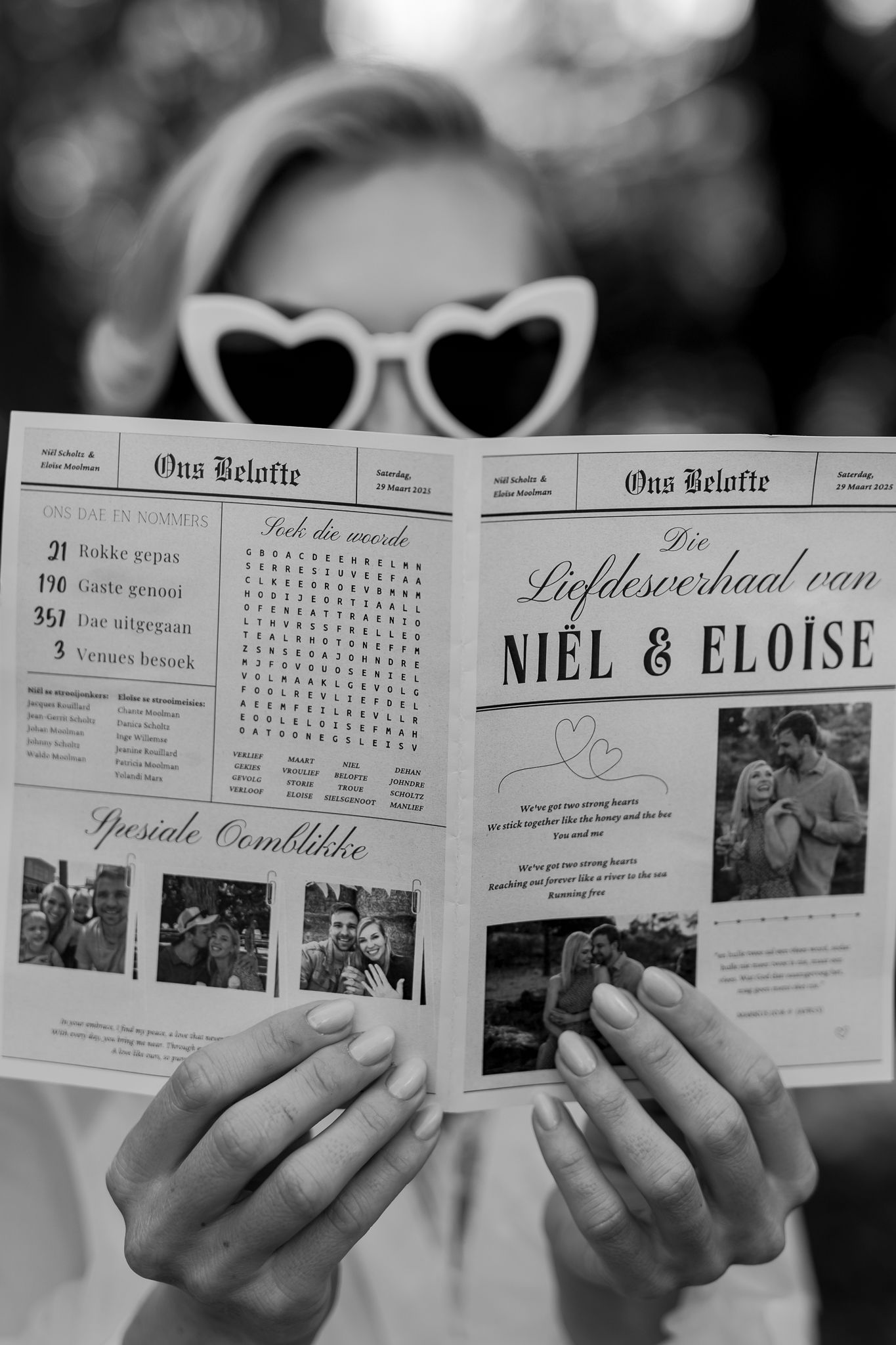 Wedding newsletter held by hands wearing heart-shaped sunglasses in black and white.