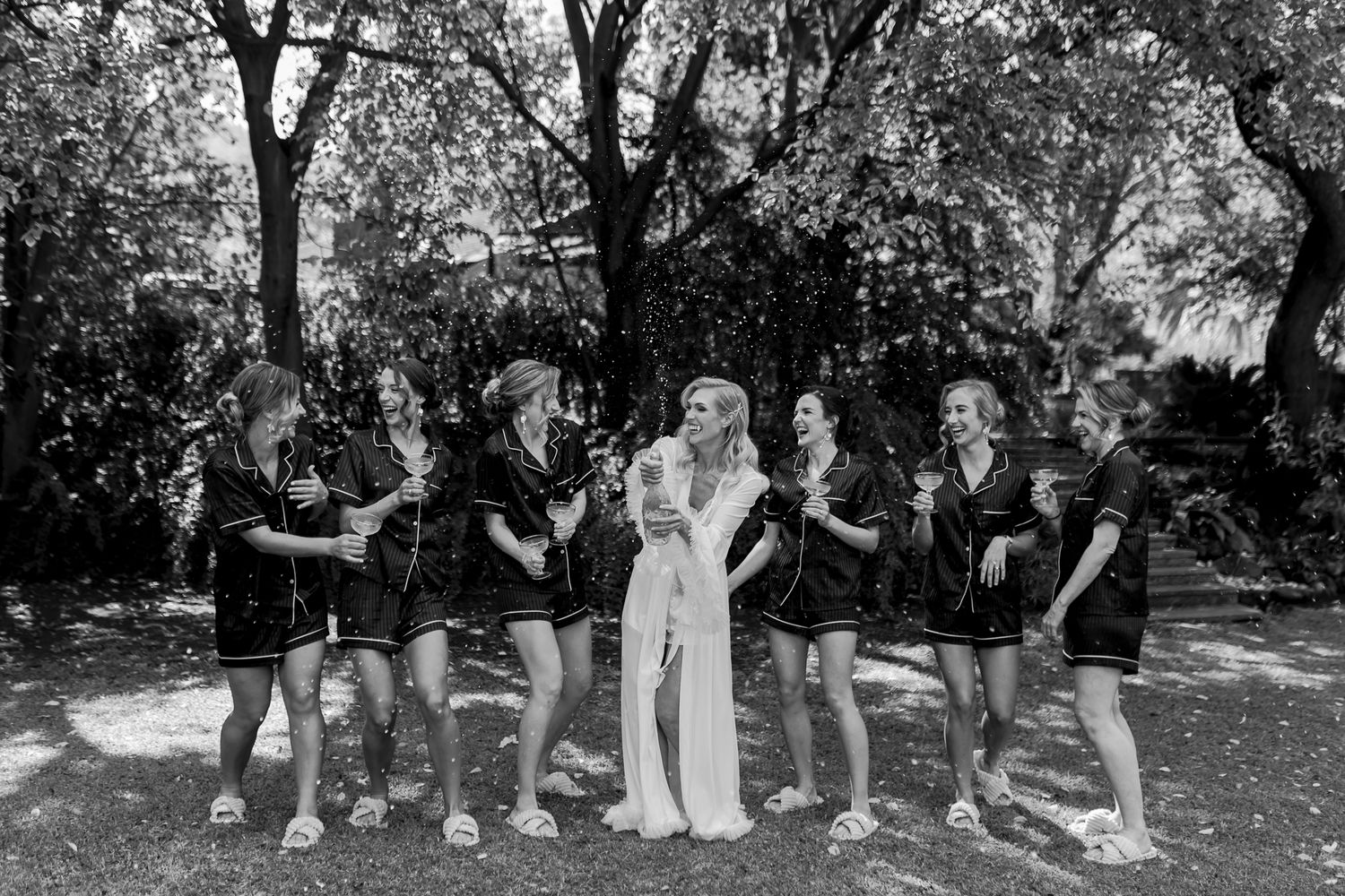 Black and white photo of bridal party in matching robes posing together outdoors.