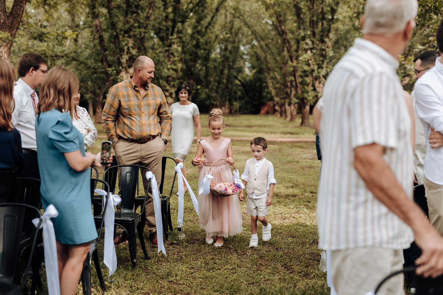 Wedding guests watch as children walk down aisle during outdoor ceremony.