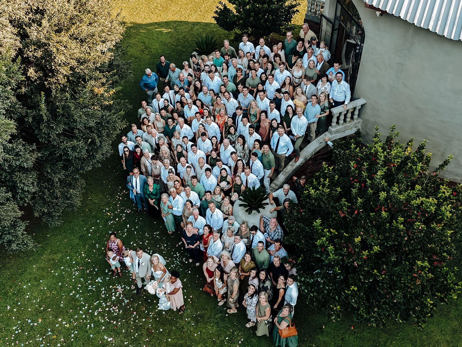 Aerial view of wedding guests arranged in a curved formation outdoors wearing coordinated blue and white attire.
