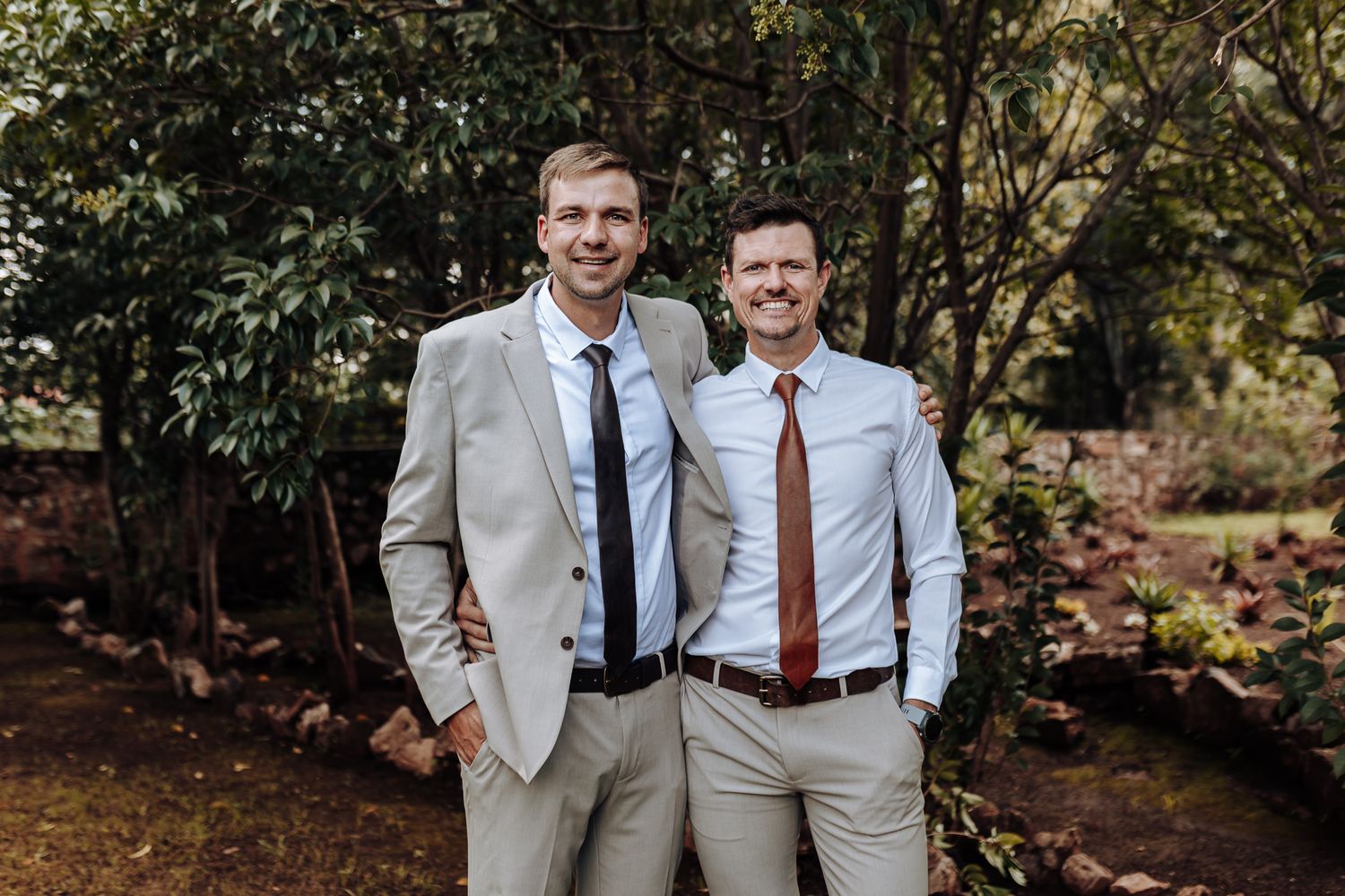 Two men in business attire standing together outdoors in a wooded setting with autumn foliage.