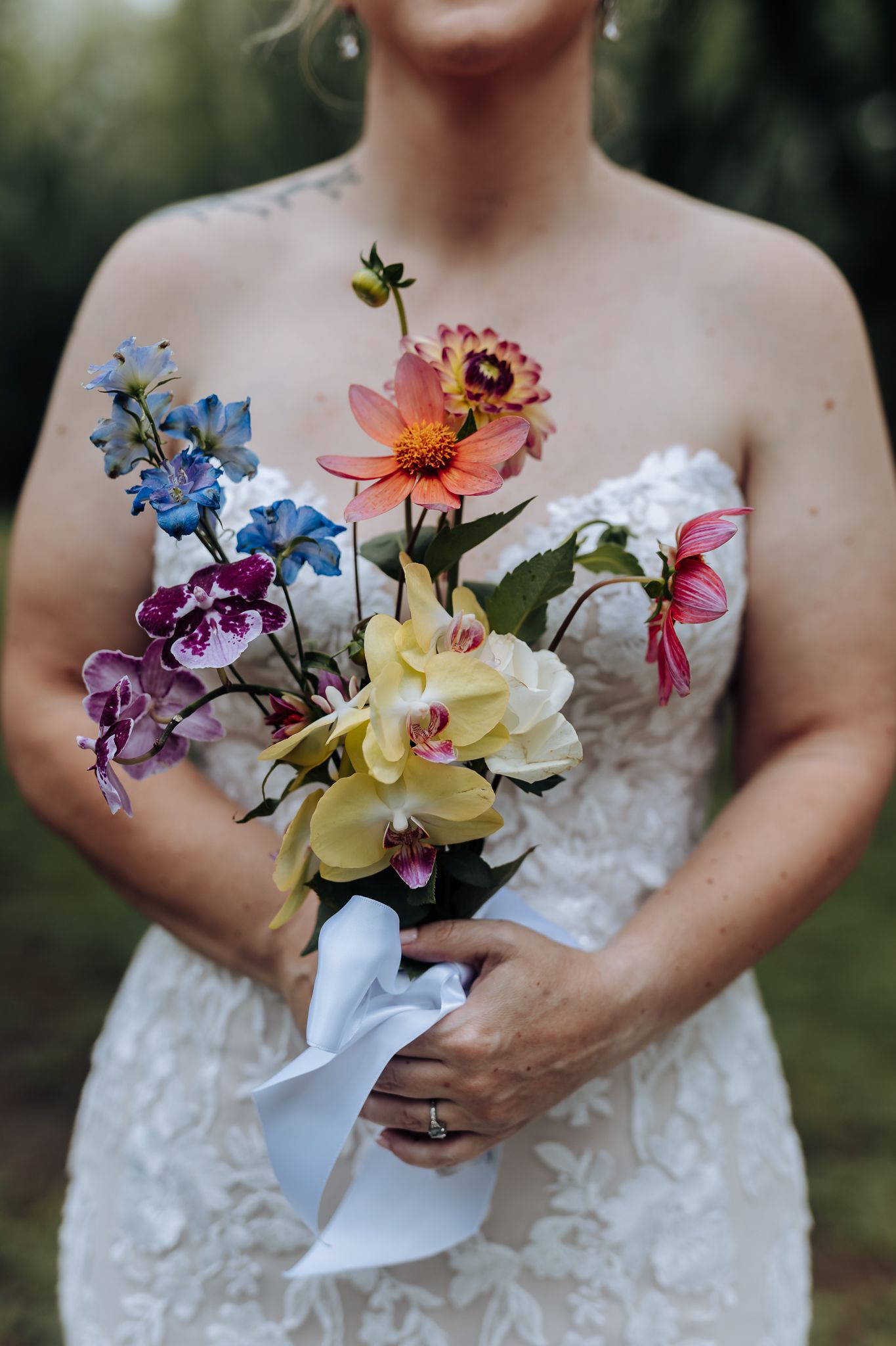 Close-up of a vibrant bridal bouquet featuring colorful orchids, daisies and delphinium wrapped with a white ribbon.
