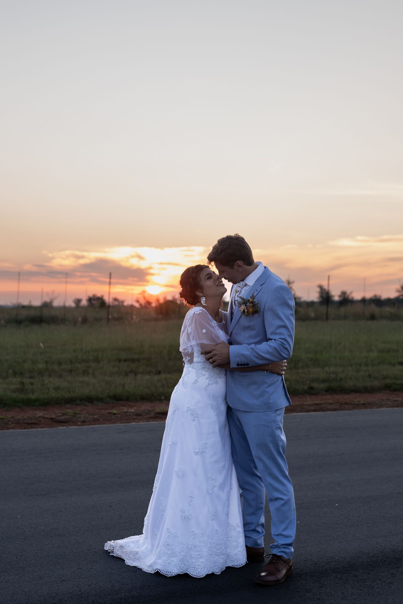 Newlyweds share romantic moment on country road during golden hour.
