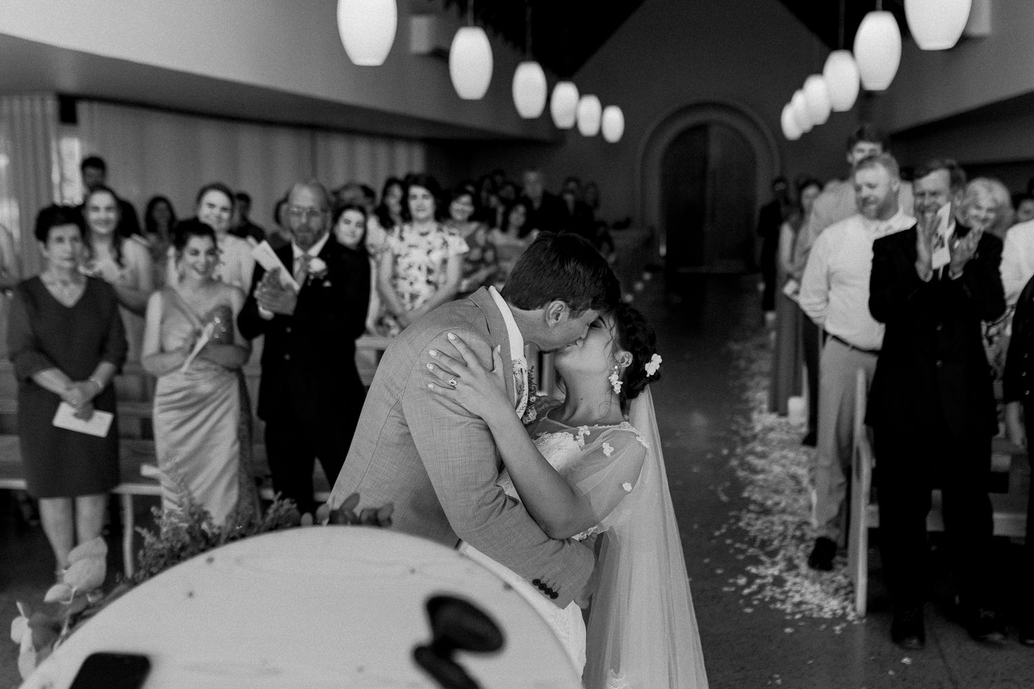 A black and white capture of a romantic first kiss during a wedding ceremony.