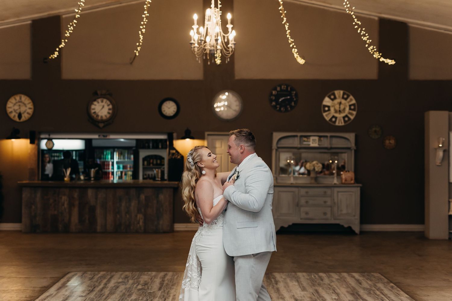 Couple shares their first dance together at a rustic wedding reception with string lights and chandeliers.