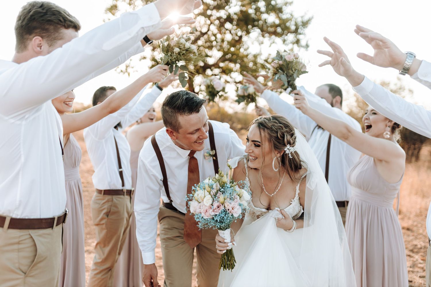 Wedding party creates tunnel of raised arms for celebratory moment outdoors.