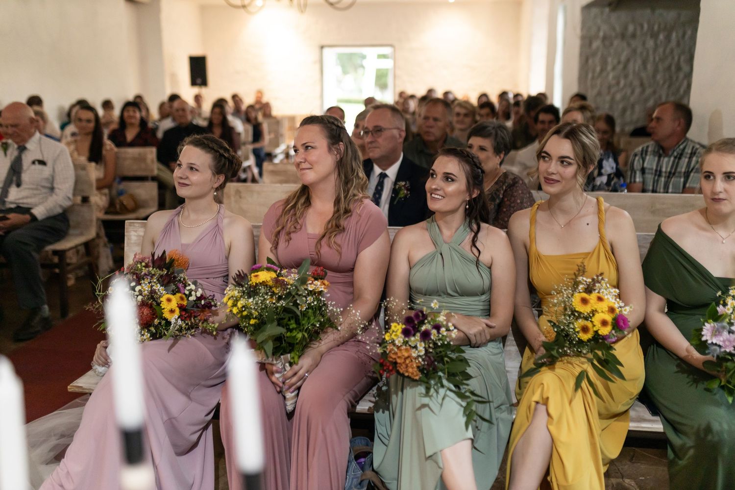 Bridesmaids in colorful dresses hold bouquets during a wedding ceremony.