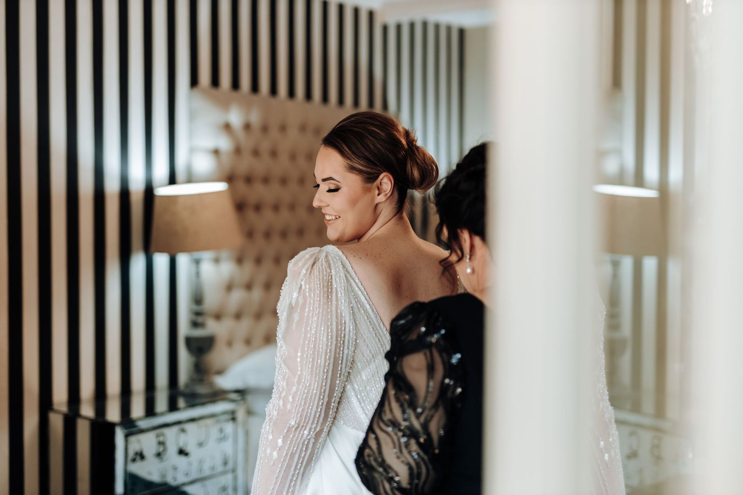 Elegant bride in long-sleeved white wedding gown being fitted before ceremony.