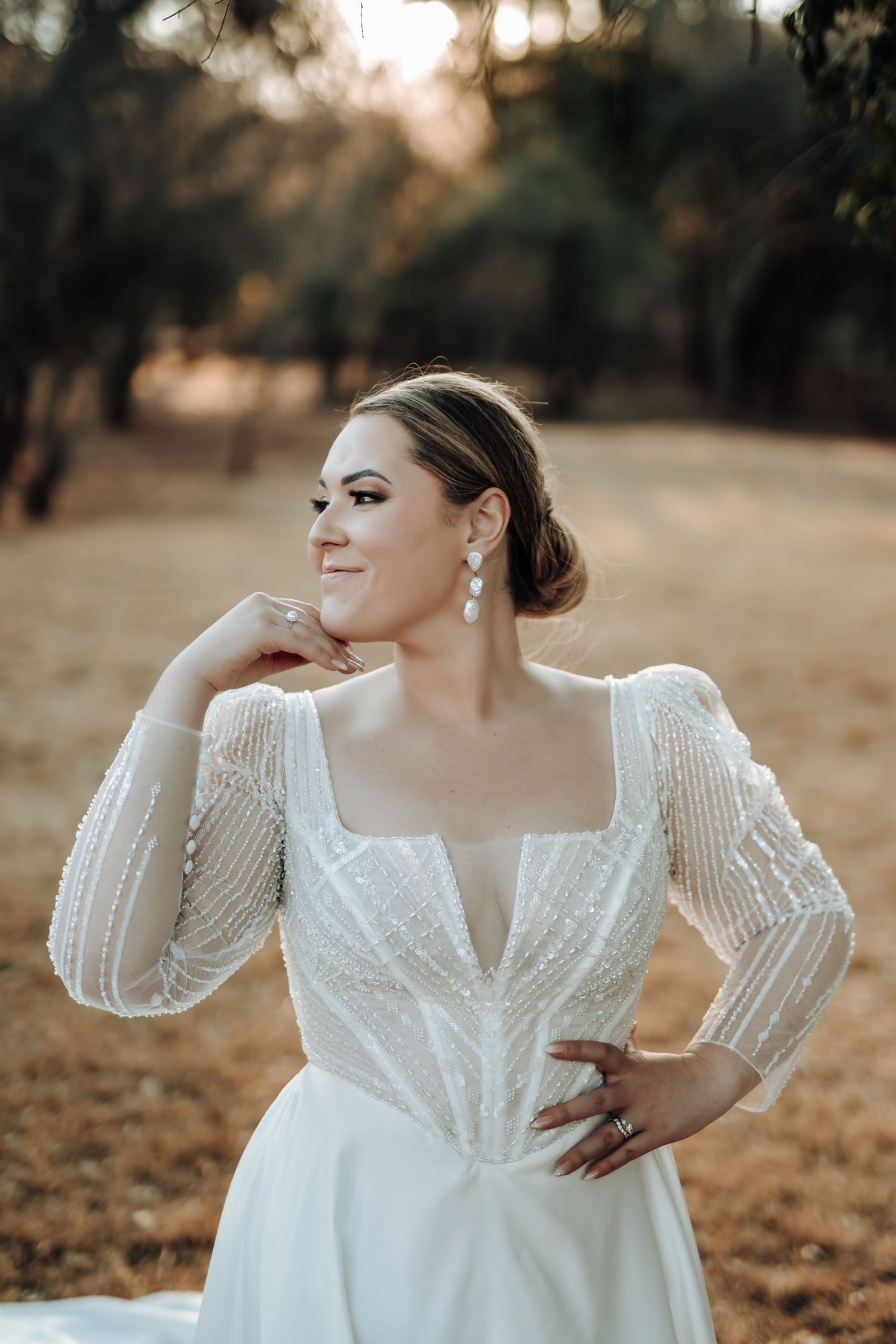 Elegant bridal portrait featuring detailed long-sleeve wedding gown in golden afternoon light.