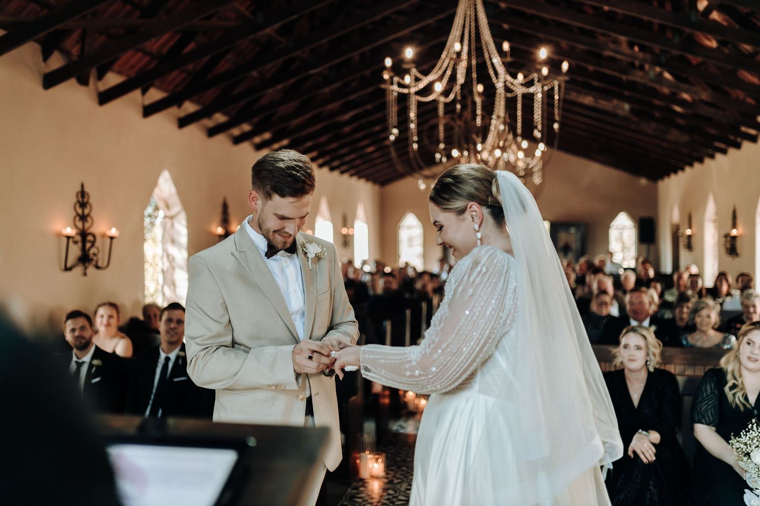 A couple exchanges rings in a traditional chapel wedding ceremony surrounded by guests.