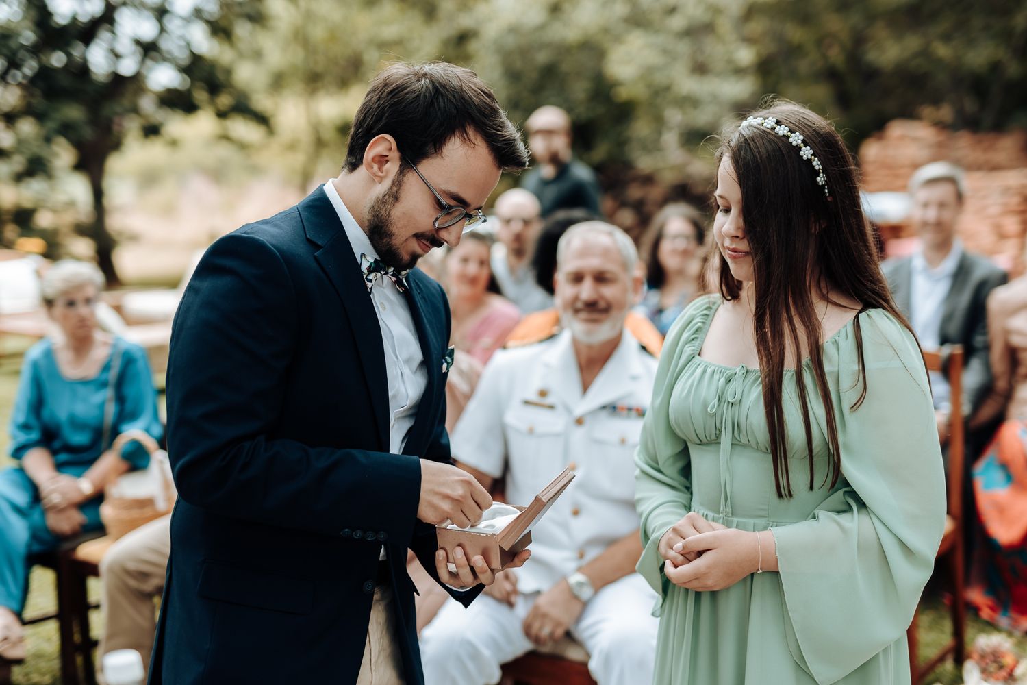 Couple exchanges rings during intimate outdoor wedding ceremony as guests look on.