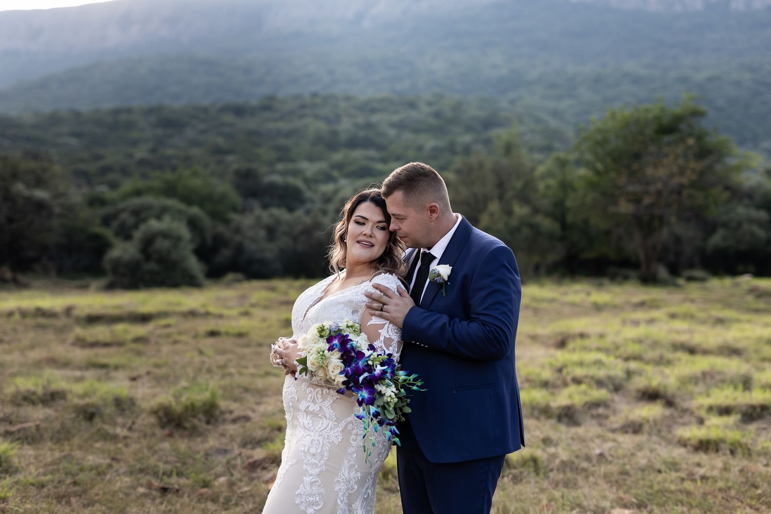 Couple embraces in scenic mountain meadow with colorful bouquet.