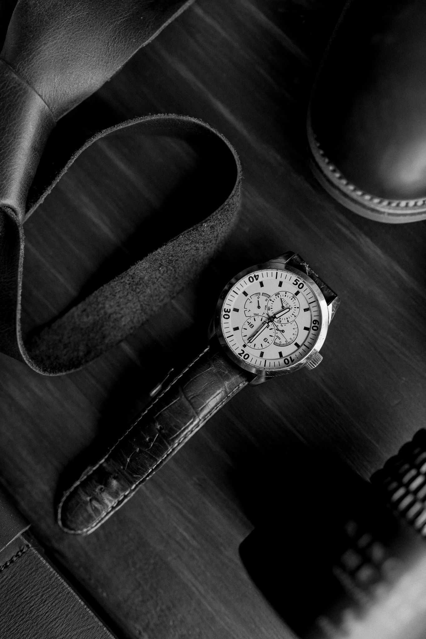 Black and white close-up of luxury watch with leather strap on dark surface.