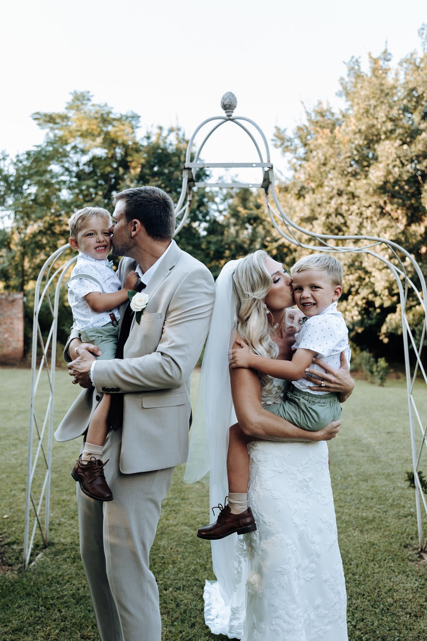 Family poses together under a decorative garden arch during a wedding.