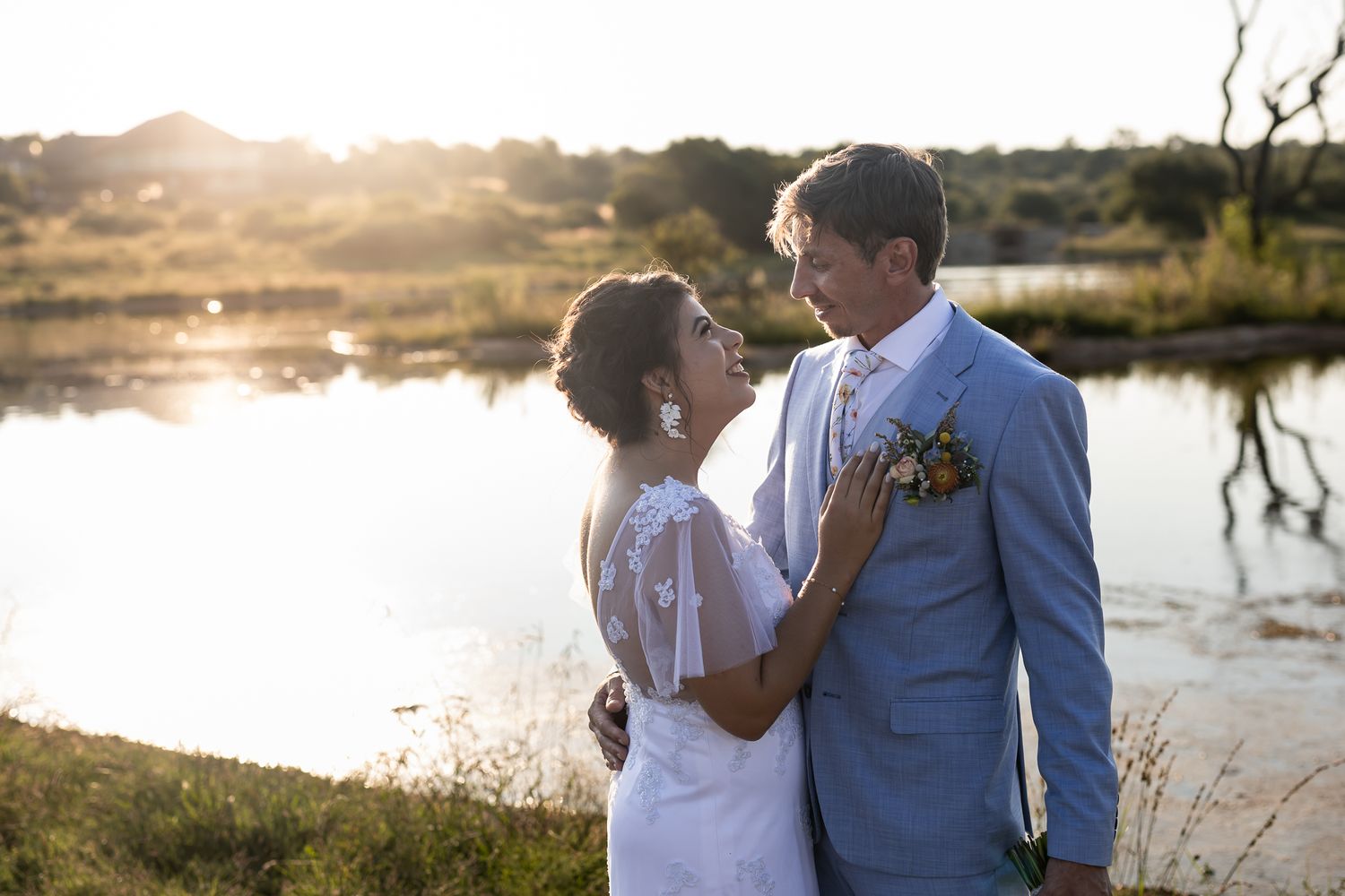 Sunset wedding portrait with couple in blue suit and white dress by water.