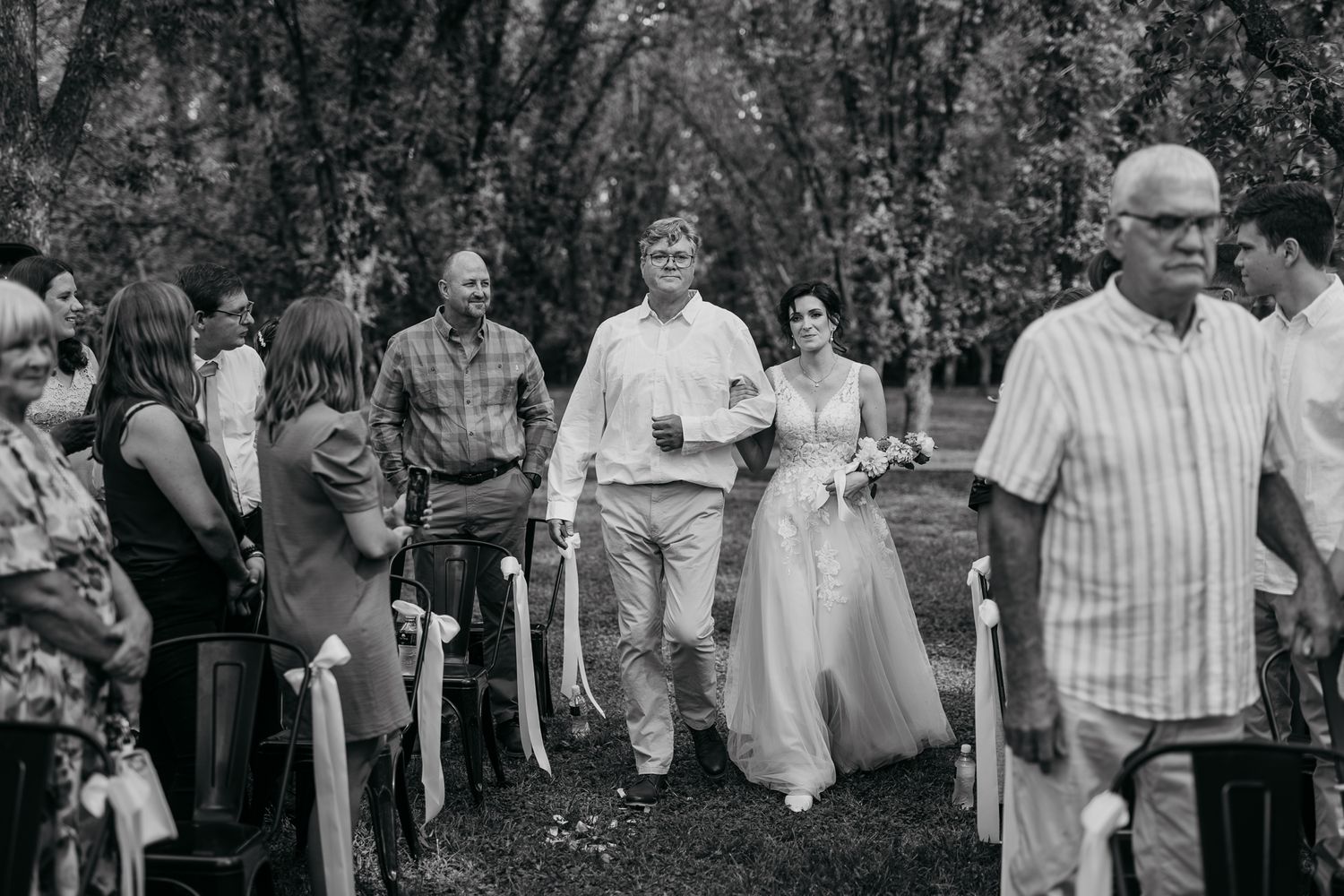 Black and white photo of wedding ceremony procession through garden with guests watching.