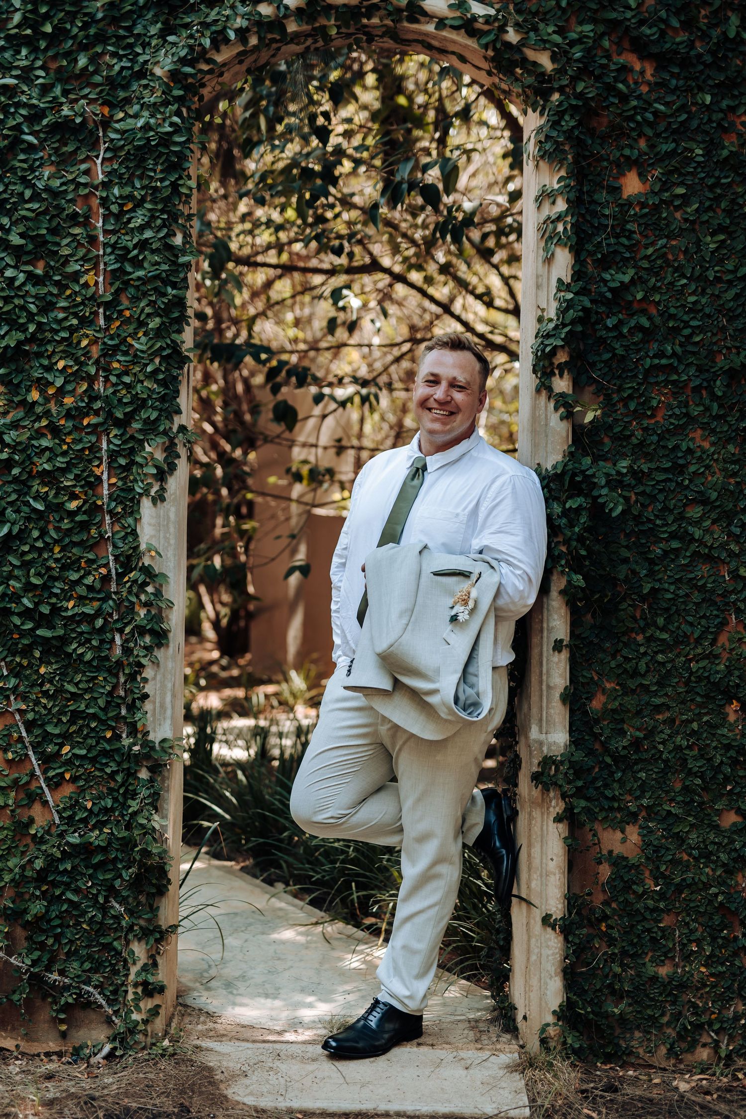 Person in formal attire poses playfully in an ivy-framed doorway outdoors.