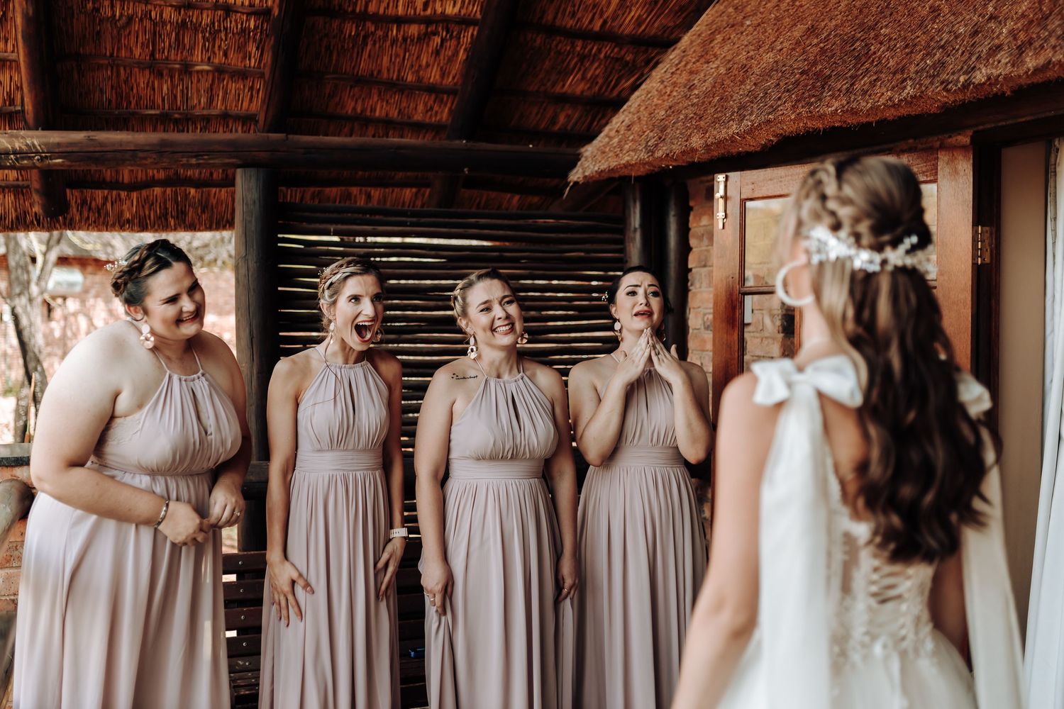 Bridesmaids in matching pink dresses have a first look moment with the bride in a rustic setting.