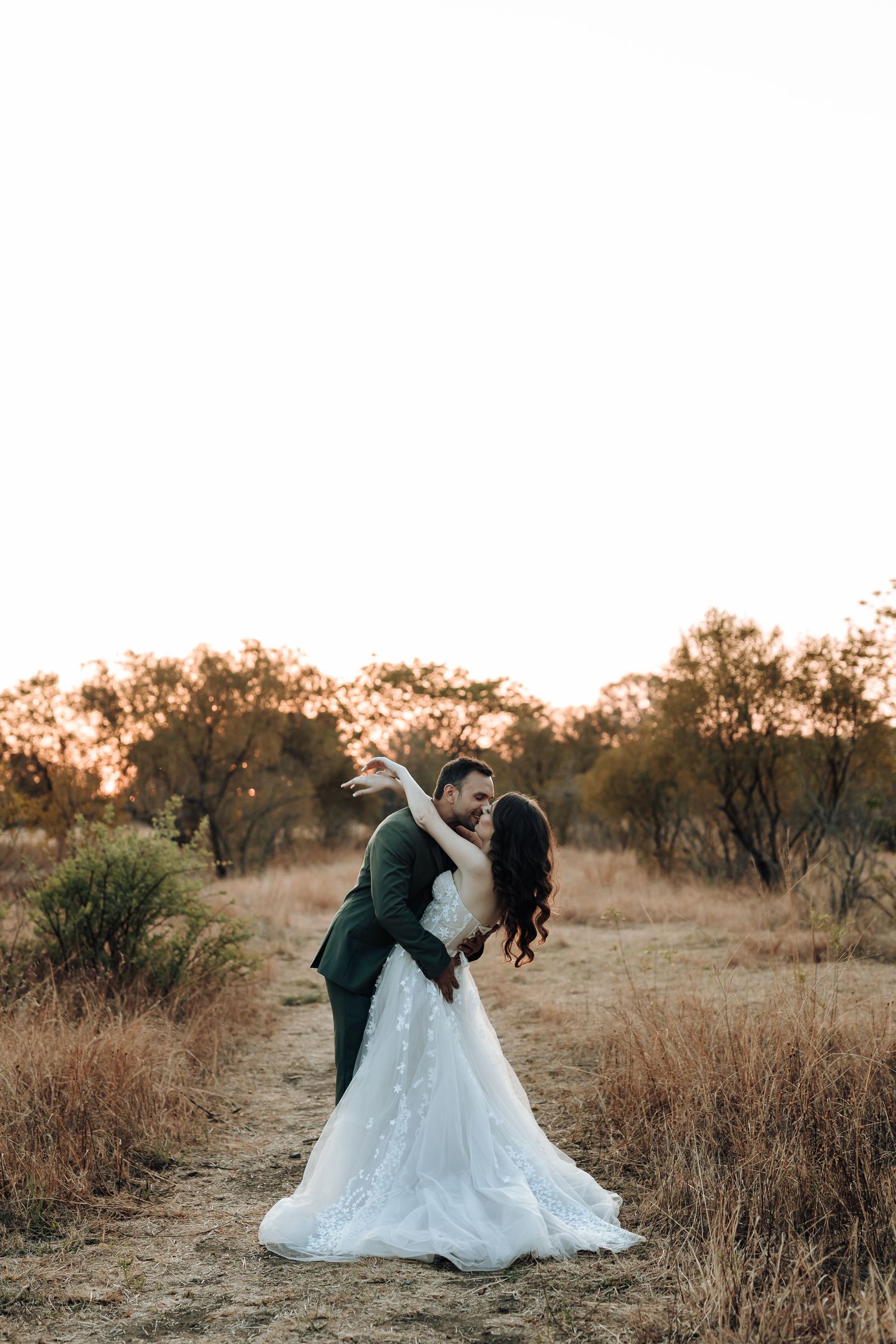 Happy newlyweds dance together on a dusty trail during sunset.
