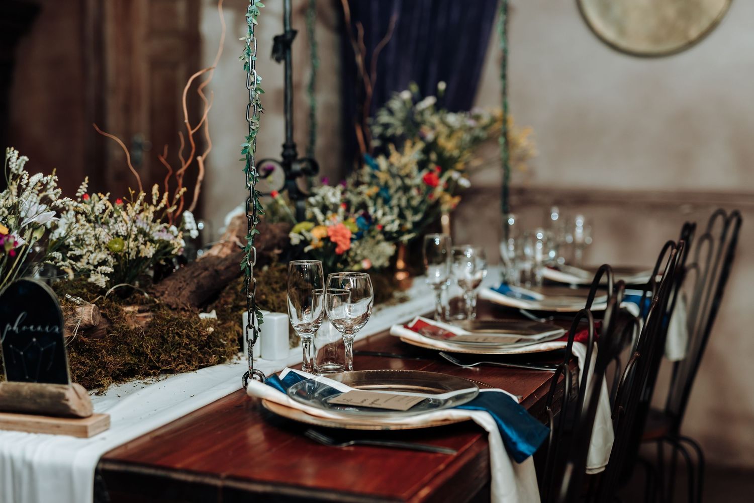 Wedding table decorated with natural greenery, blue accents, and vintage place settings.