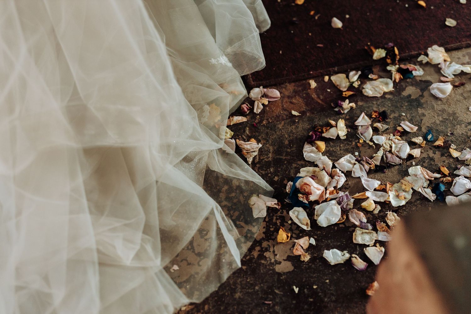 White wedding dress train with scattered flower petals on dark wooden floor.