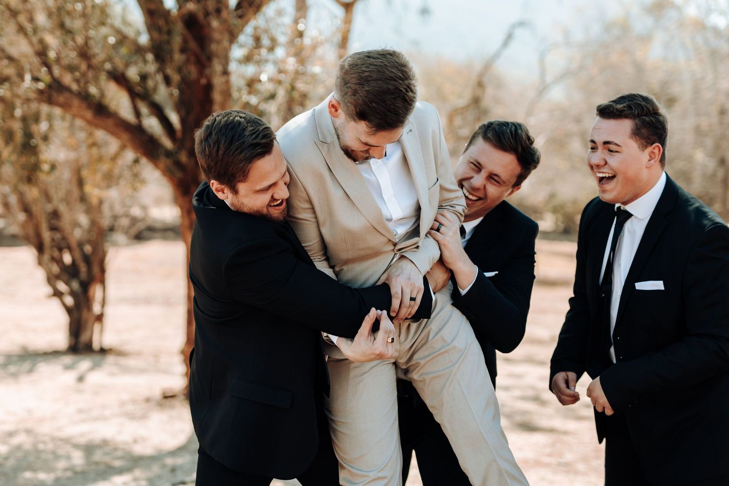 Wedding party shares a lighthearted moment lifting and laughing with the groom.