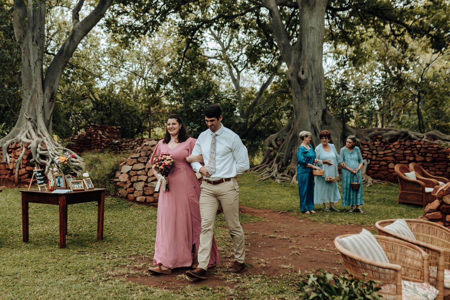 Outdoor wedding celebration with guests in formal attire walking along a garden path.
