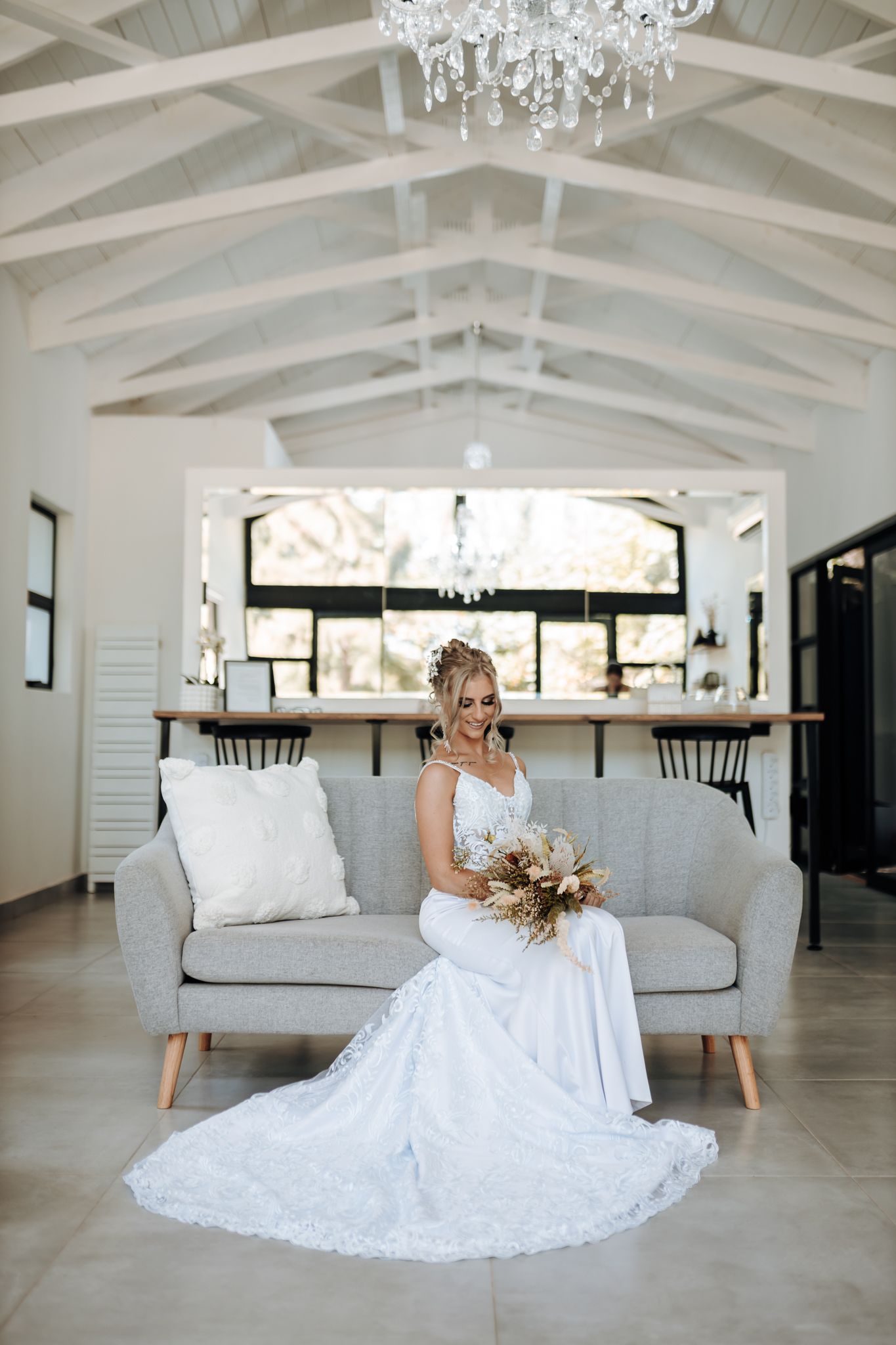 Wedding dress with lace train elegantly draped around modern couch in bright white venue.