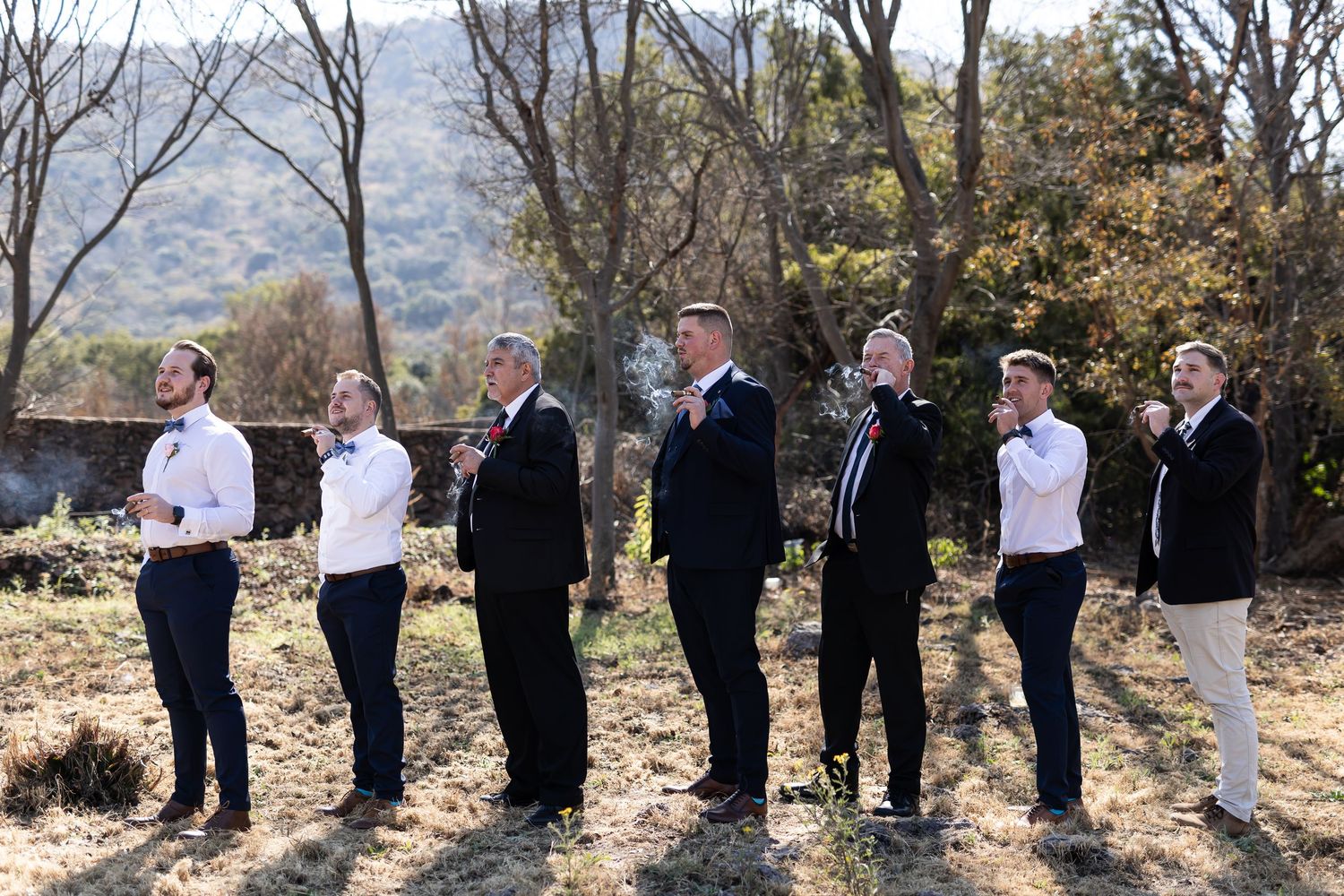 Group portrait of wedding party standing in line on a hillside with mountains and autumn trees in the background.