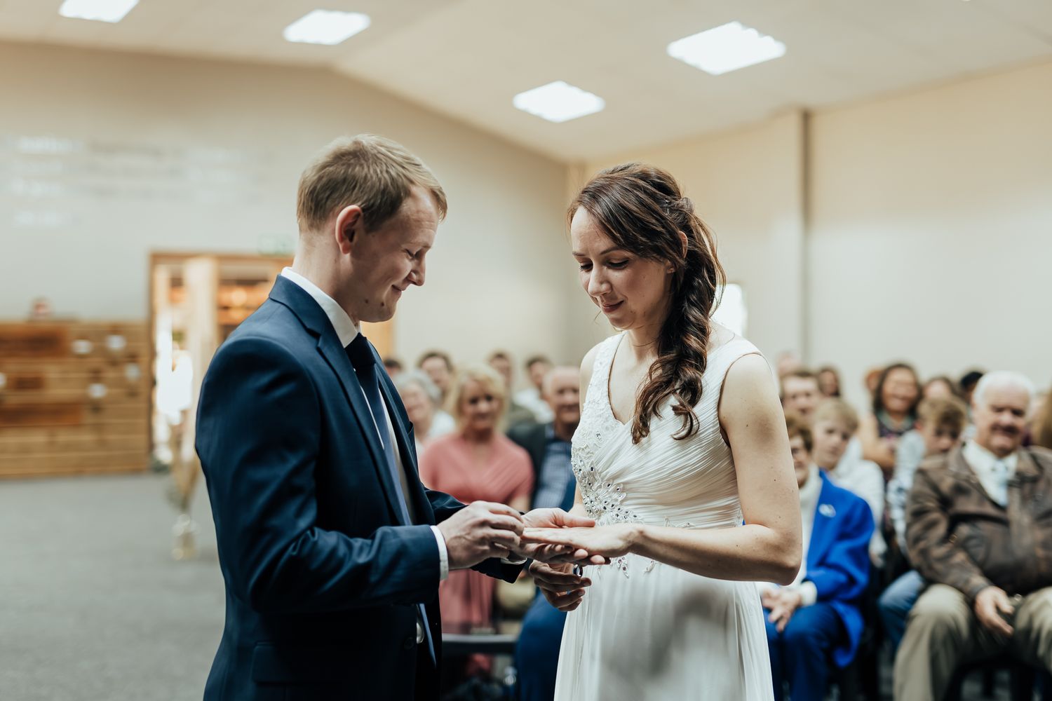 Indoor ceremony featuring an exchange of rings between a couple wearing formal wedding attire.