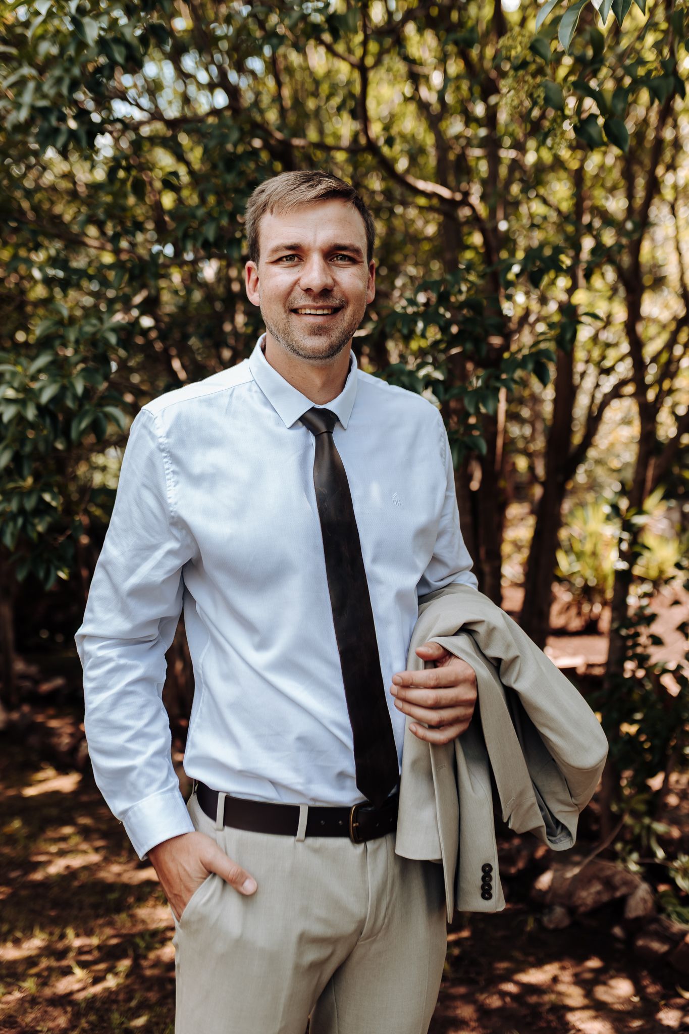 Business portrait of man in white shirt and dark tie holding light jacket outdoors.