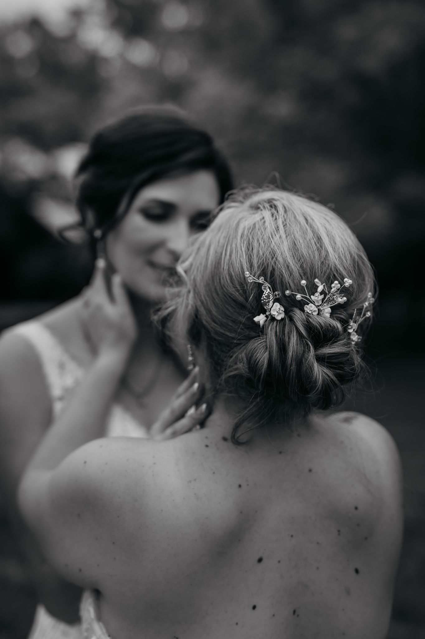 Close-up black and white photo of delicate floral hairpiece detail in an updo hairstyle at a wedding.