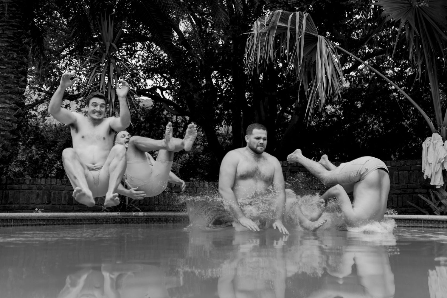 Black and white photo of groomsmen relaxing poolside during wedding celebrations.