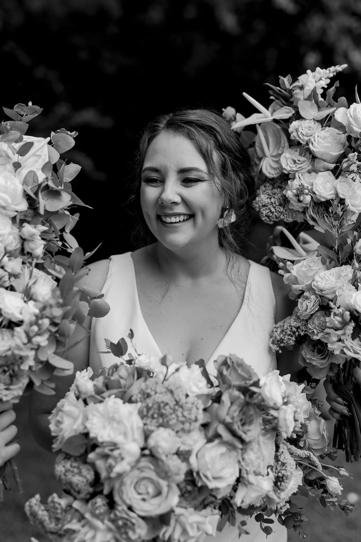 Black and white portrait of a joyful bride surrounded by elegant floral arrangements.