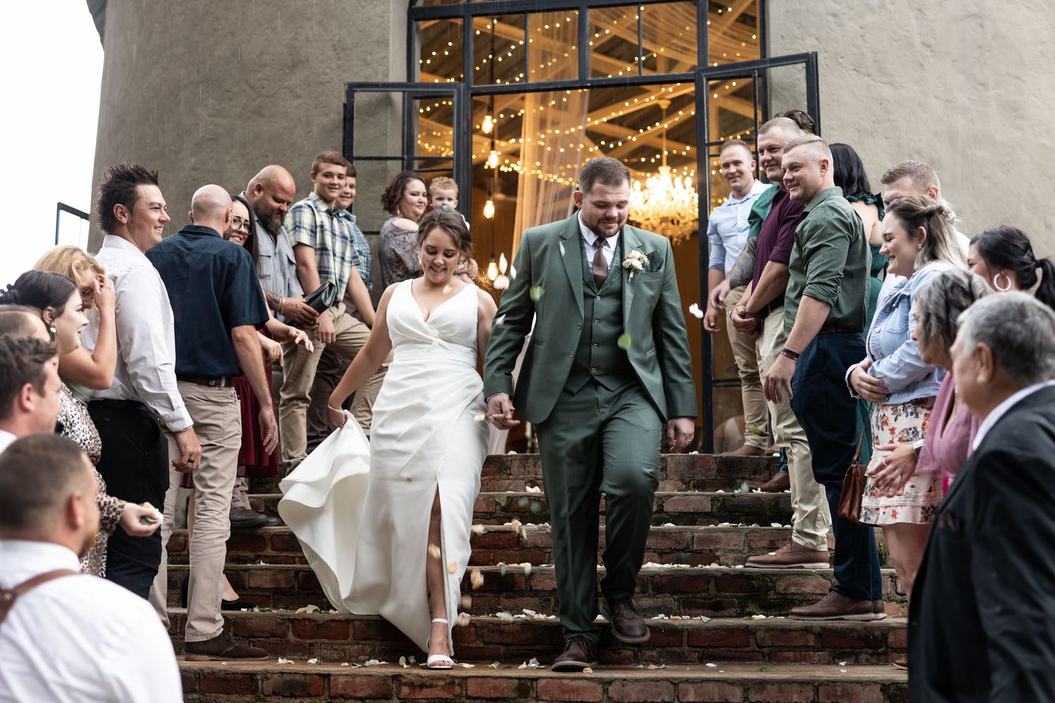 Newlyweds exit down stone steps while wedding guests line both sides in celebration.