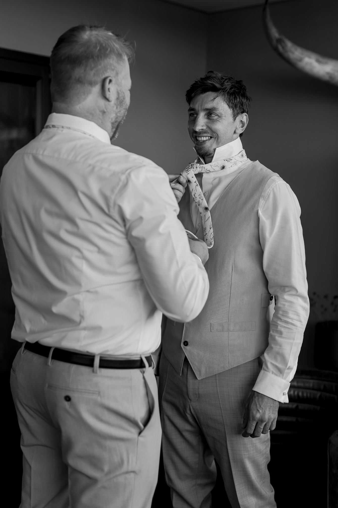 Two people in formal wear adjusting a tie during wedding preparations.