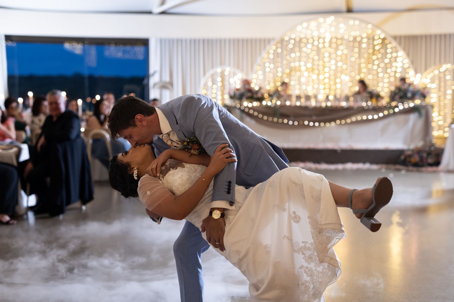 A dramatic wedding dance dip move performed on a misty dance floor with string lights overhead.