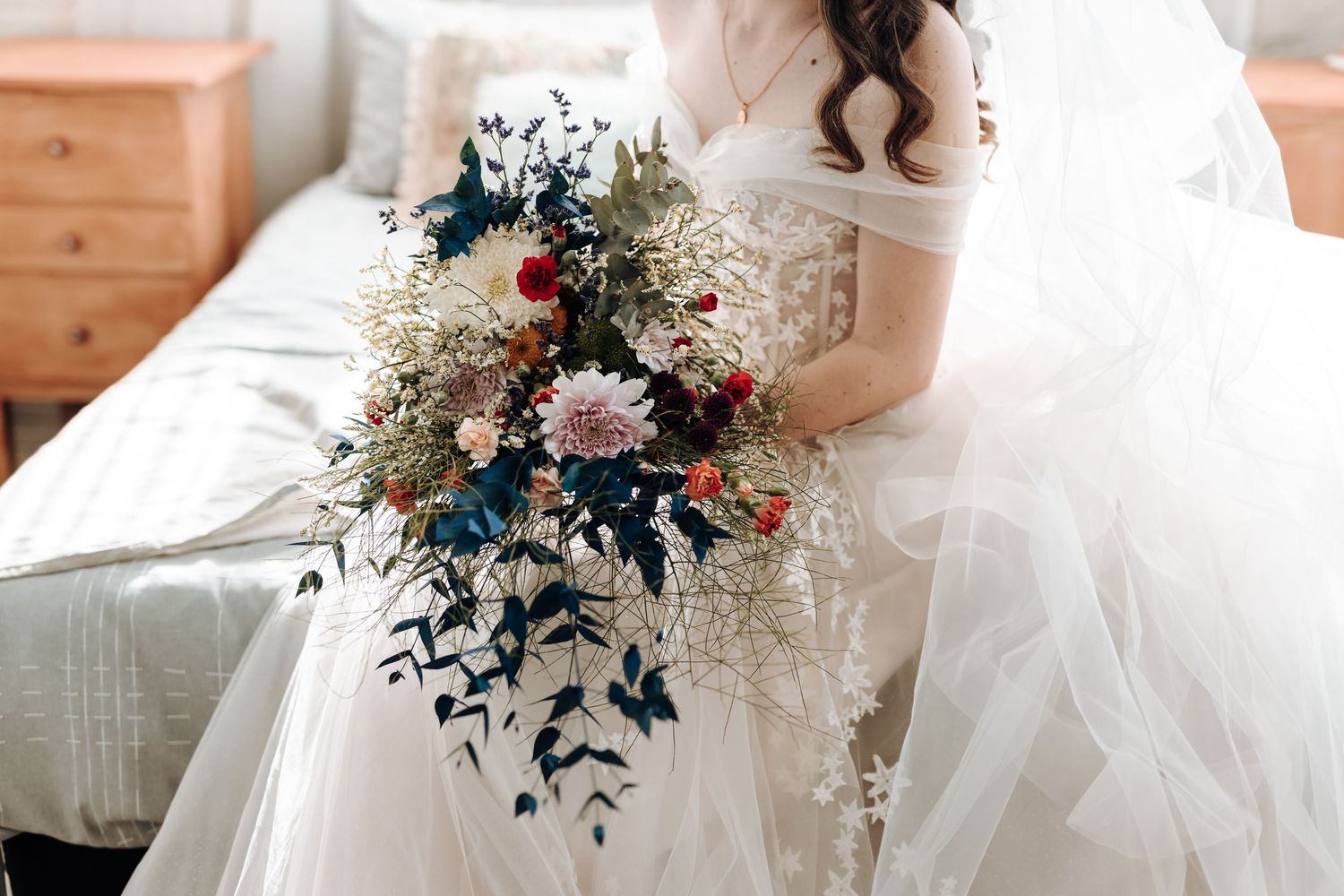 Detail shot of cascading bridal bouquet with navy, pink and white flowers against wedding dress.