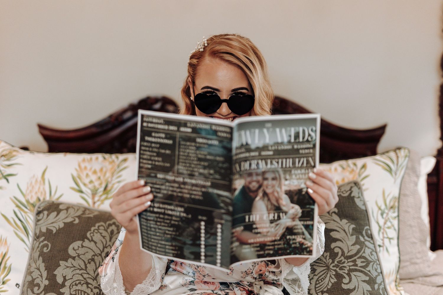 Person in sunglasses reads magazine while relaxing on decorative pillows.