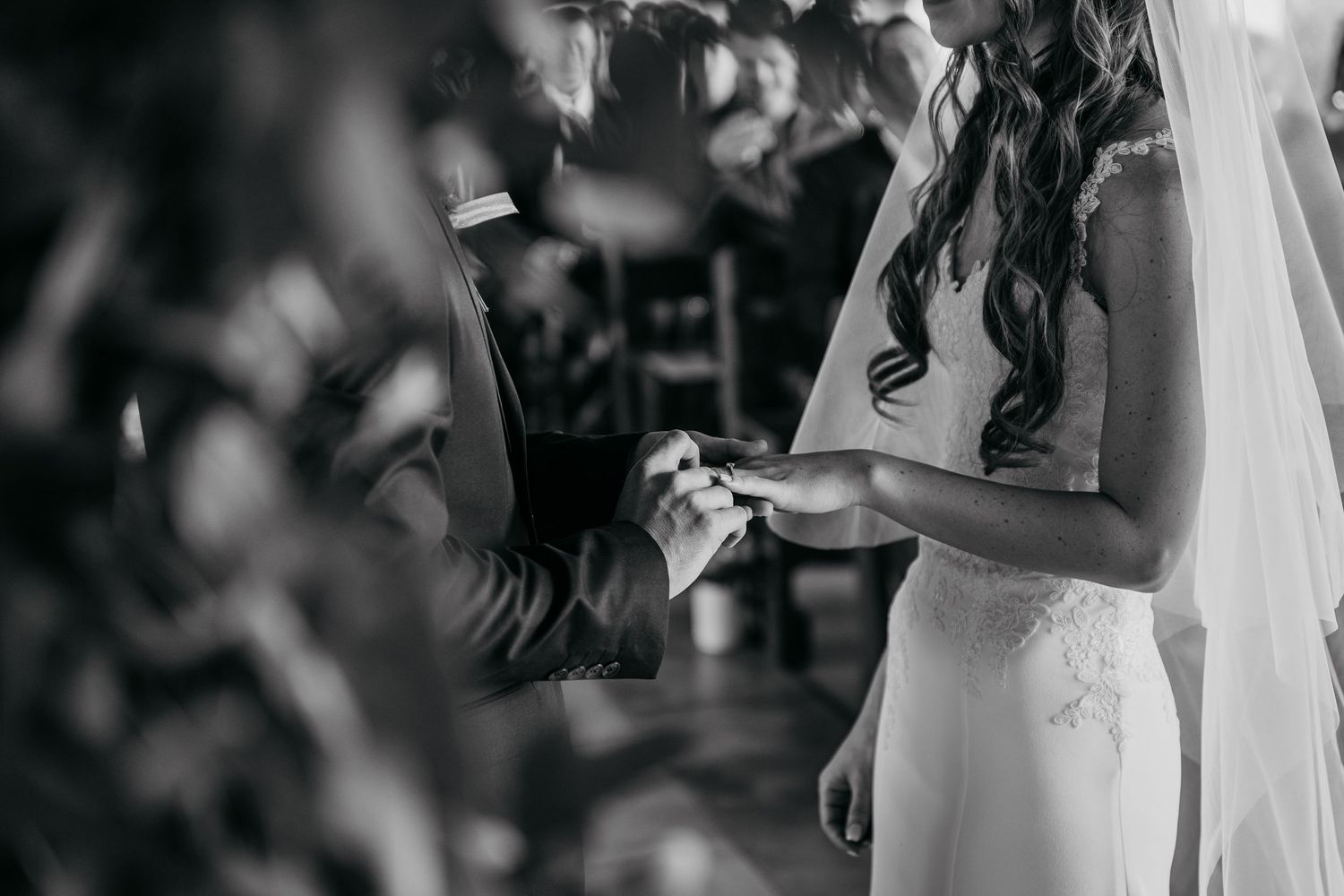 Black and white image of a couple exchanging rings during wedding ceremony.